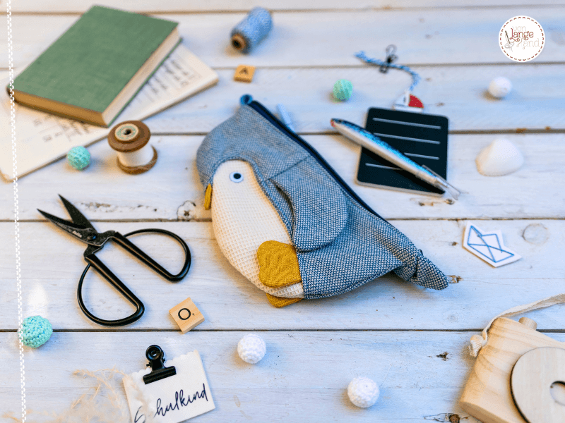 praktische Geschenke zur Einschulung wie Stifte und Mäppchen liegen auf einem weißen Holztisch