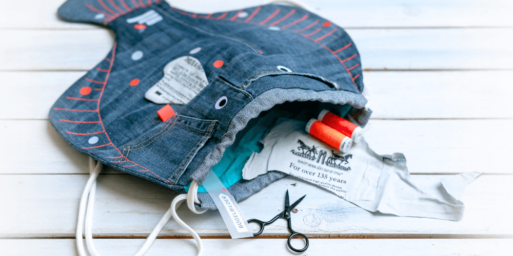 Rucksack-Scholle aus alter Jeans genäht liegt auf weißem Holzuntergrund